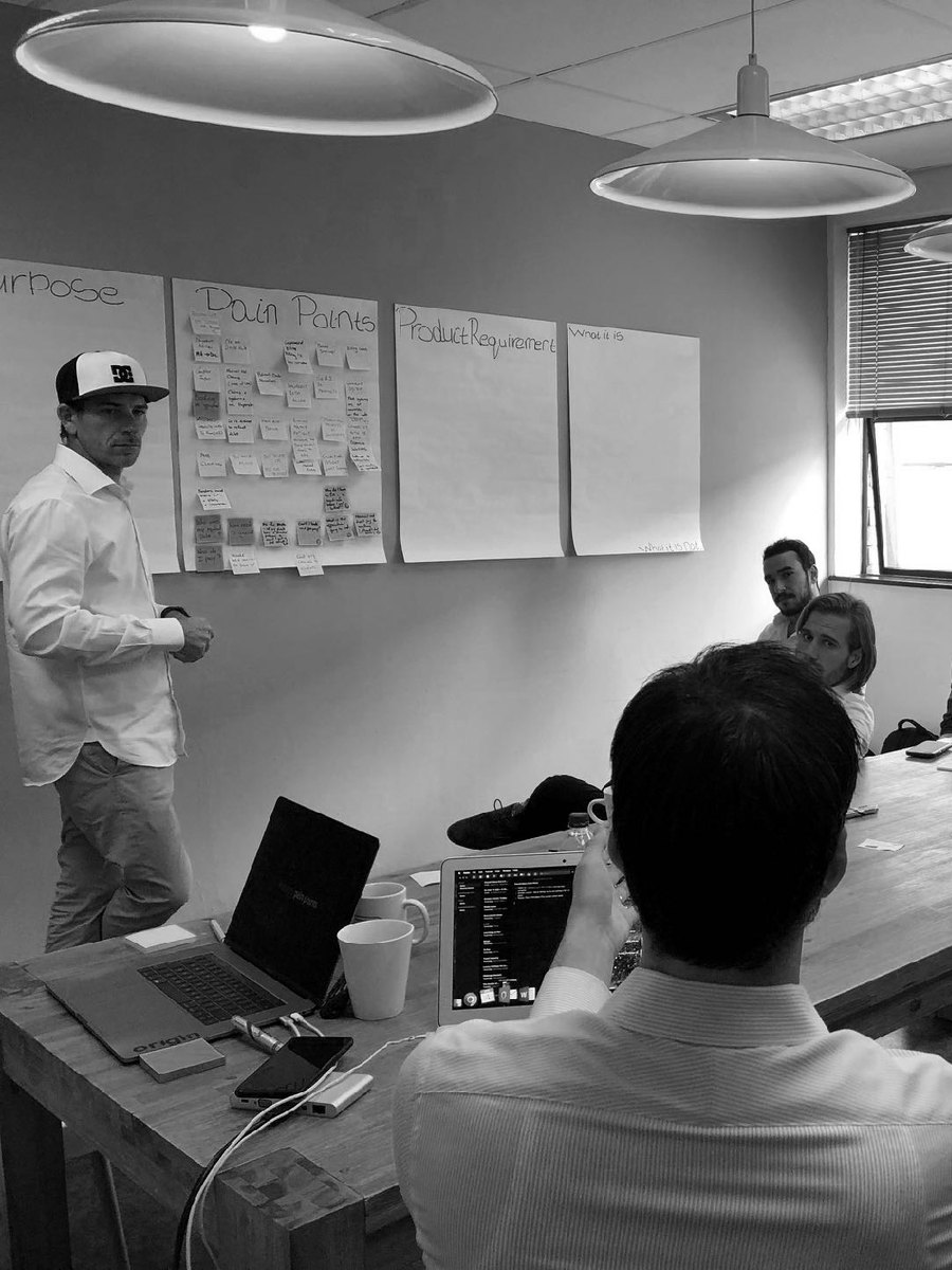 The requirements workshop in progress: a facilitator standing beside flip-chart sheets headed Pain Points and Product Requirements, with the client team seated around a table.