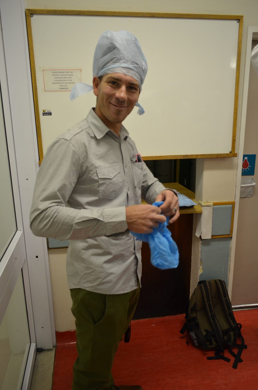 A staff member gowning up in theatre, cap and gloves on, beside a blank whiteboard.