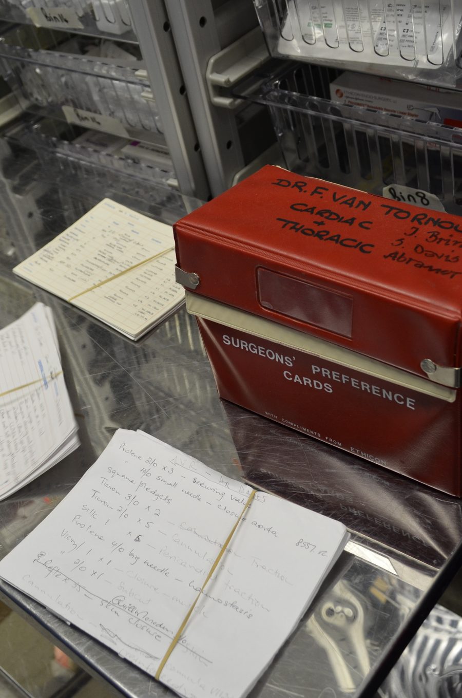 A red box labelled Surgeons' Preference Cards beside handwritten instrument lists on a stainless steel trolley.