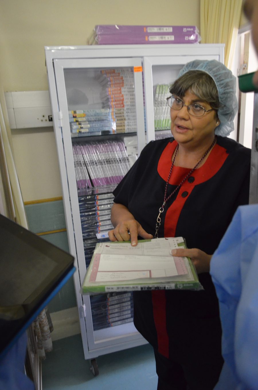 A staff member holding a patient chart in front of a locked medicine cabinet, talking to a colleague.
