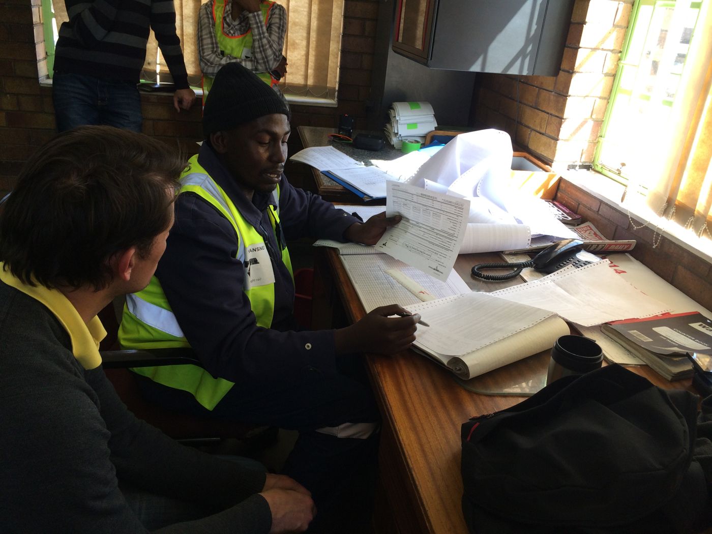 Foremen reviewing paper logs together at a control-point desk.
